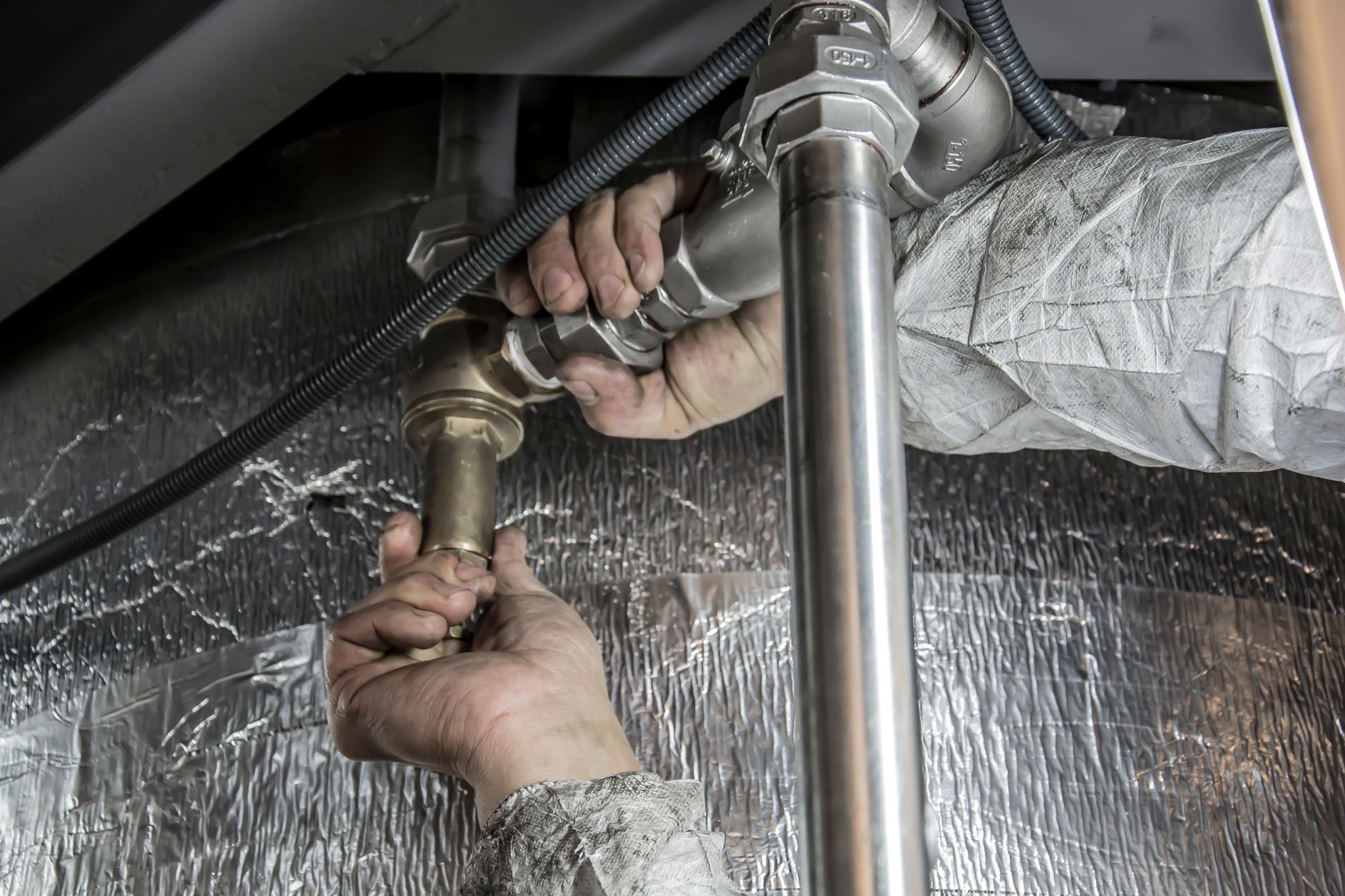 Plumber in shoe covers tightening a shutoff valve under a kitchen sink in a Colorado Springs home